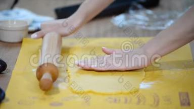 女人`手把面团擀在厨房的桌子上。